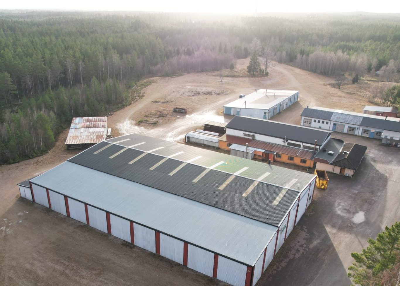 Vy av ett stort industriområde med flera byggnader och omgiven av skog.