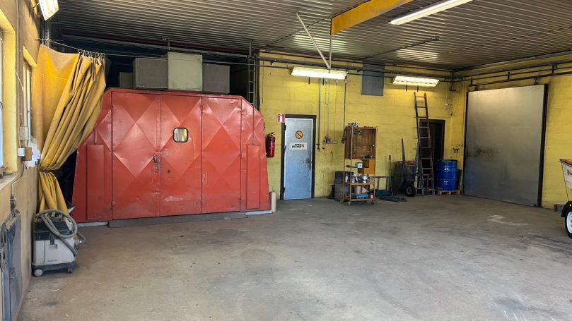 Verkstad med gula väggar, röd säkerhetsdörr och verktyg i bakgrunden.