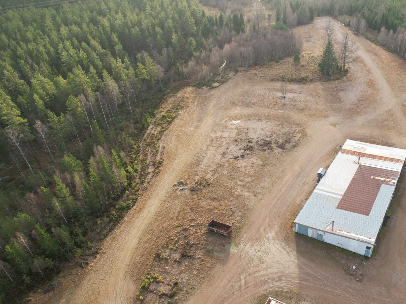 Landskap med en grusväg, skog i bakgrunden och en byggnad till höger.