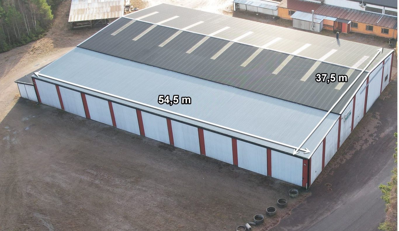 Lagerbyggnad med röd fasad och platt tak, omgiven av grus och fordon.